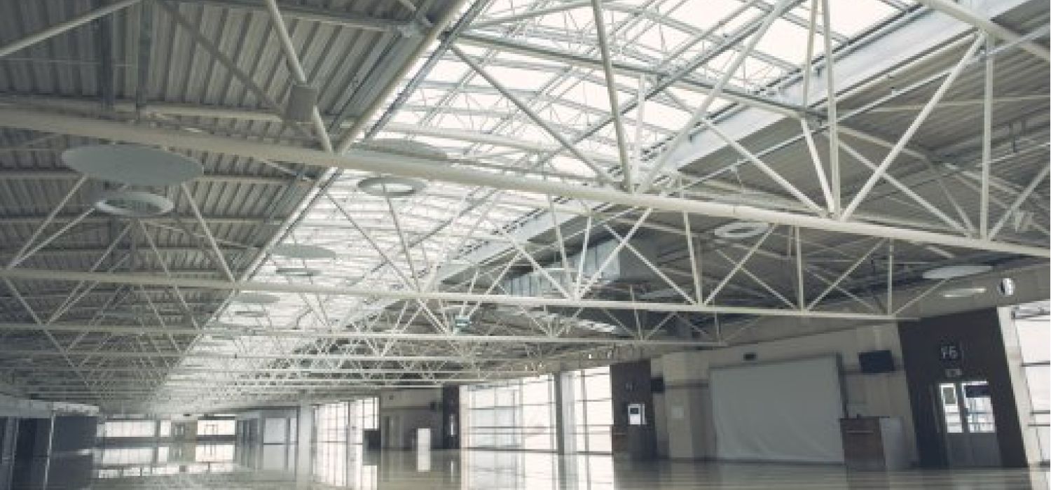 Interno di un grande spazio commerciale o fieristico vuoto con soffitto a tralicci metallici e ampie vetrate che diffondono luce naturale